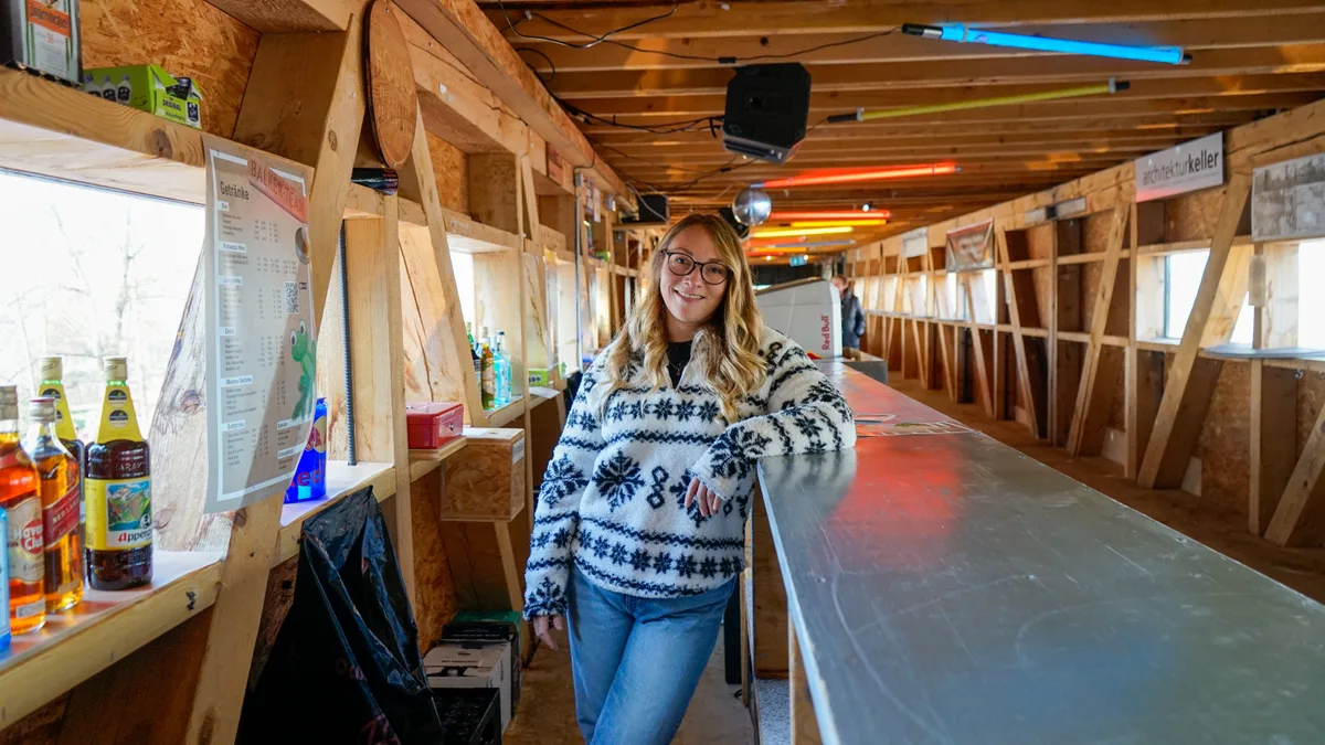 Man sieht eine junge Frau in einer Bar aus Holz.